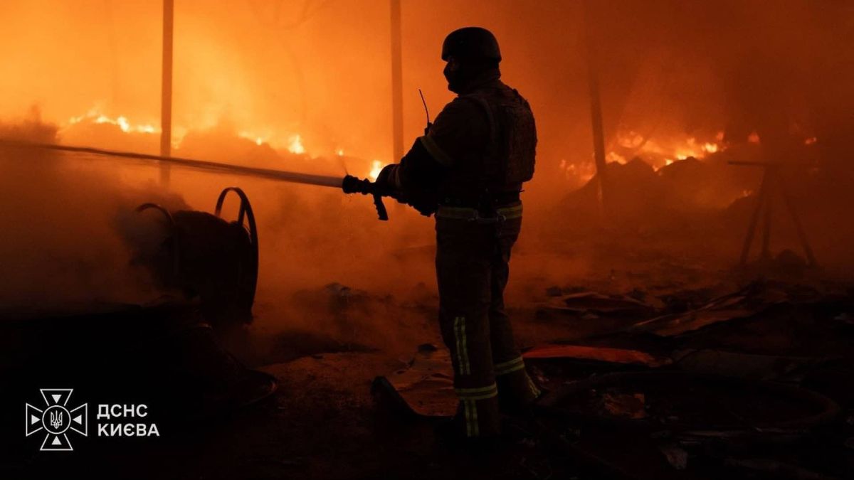 Рятувальник ДСНС з пожежним рукавом гасить сильну пожежу у складському приміщенні вночі в Києві.