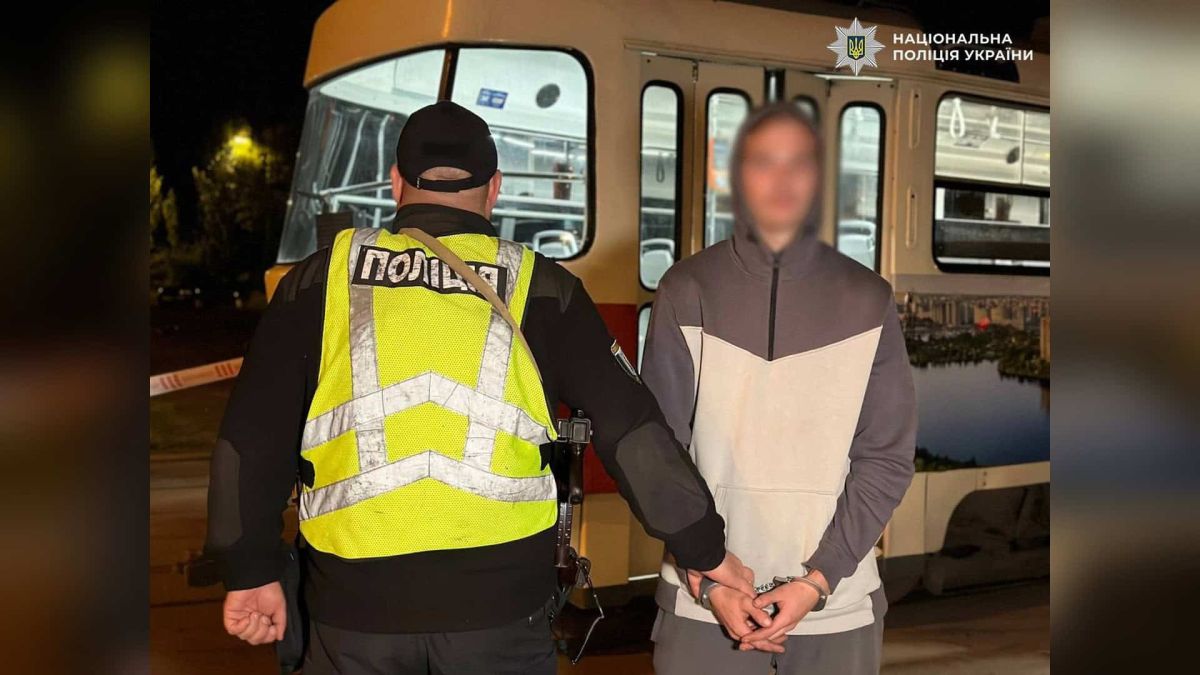 Поліцейський Києва веде затриманого 20-річного чоловіка в кайданках біля трамвая, яким той заволодів у нетверезому стані