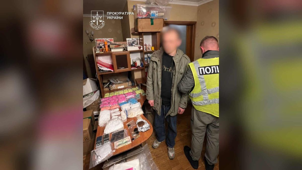 Поліцейський поруч із підозрюваним біля столу з пакетами пігулок і порошків, вилучених в орендованій квартирі в Києві