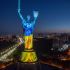 Підсвічений синьо-жовтими кольорами монумент «Батьківщина-Мати» вночі на тлі нічного Києва та автомагістралі