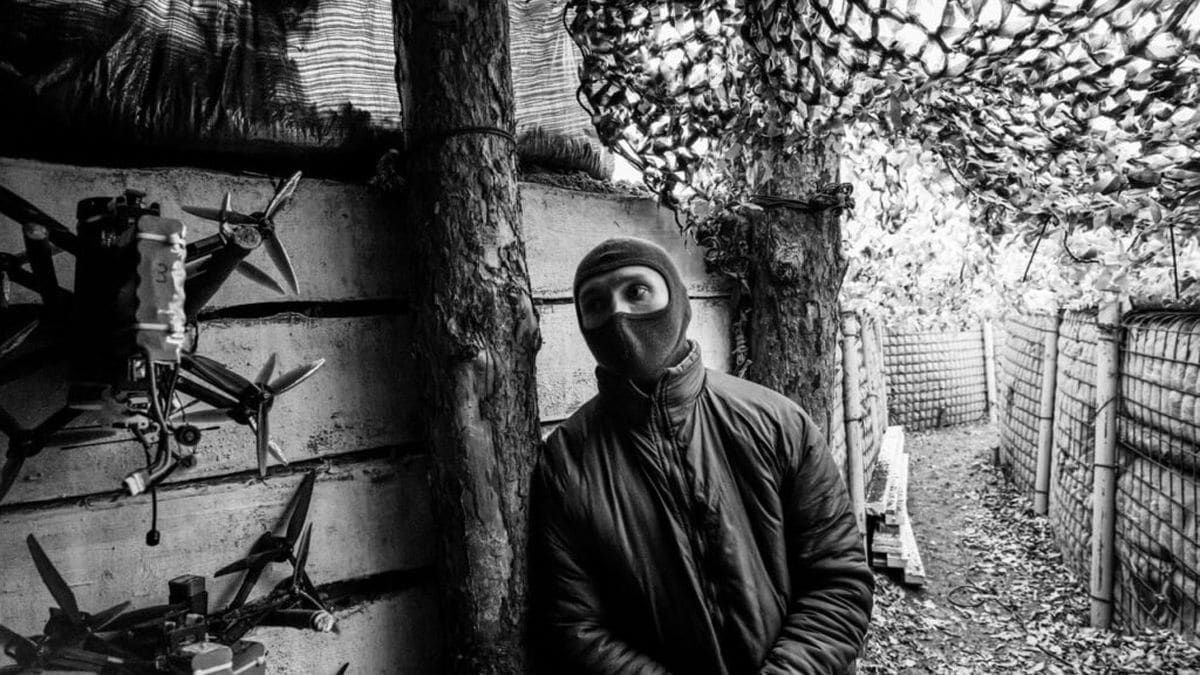 Чорно-біле фото військового у балаклаві в укріпленому бліндажі з дронами