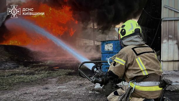 Рятувальник ДСНС Київщини спрямовує потужний струмінь води на високе полум'я під час гасіння масштабної пожежі в Бориспільському районі