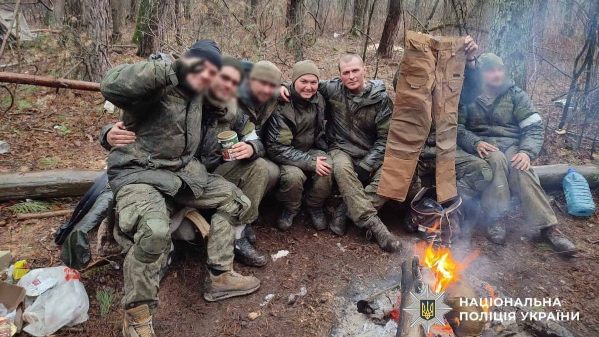 Російські солдати в камуфляжі сидять на колоді біля вогню в лісі
