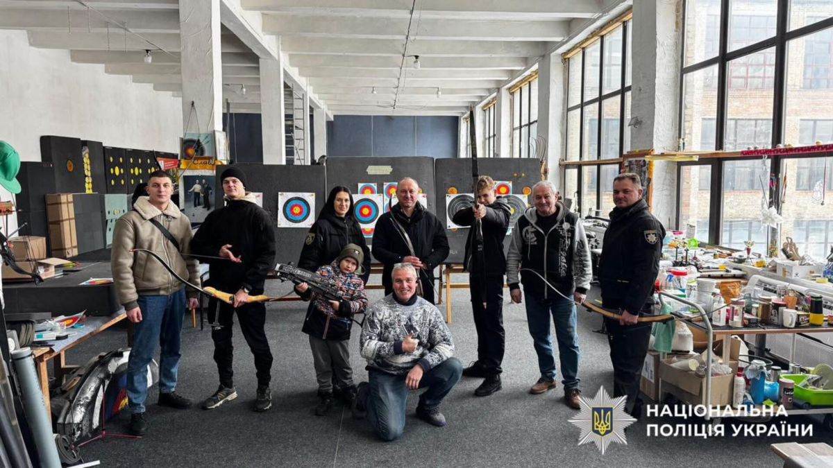 Група поліцейських-ветеранів з луками позують у тирі для стрільби з лука, на фоні мішені та обладнання
