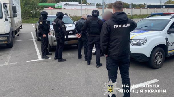 Команда правоохоронців проводить затримання підозрюваного на вулиці біля стоянки автомобілів
