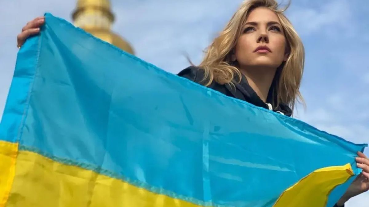 Акторка Кетрін Винник тримає синьо-жовтий прапор України на тлі золотого купола храму в Києві