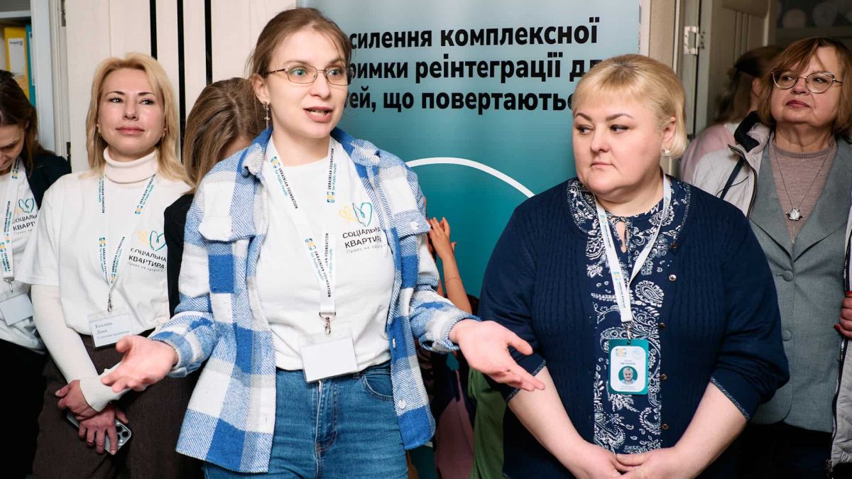 Учасниці відкриття соціальної квартири у Києві для юнаків з окупованих територій — жінки з бейджами «Соціальна квартира» на тлі банеру проєкту Bring Kids Back UA