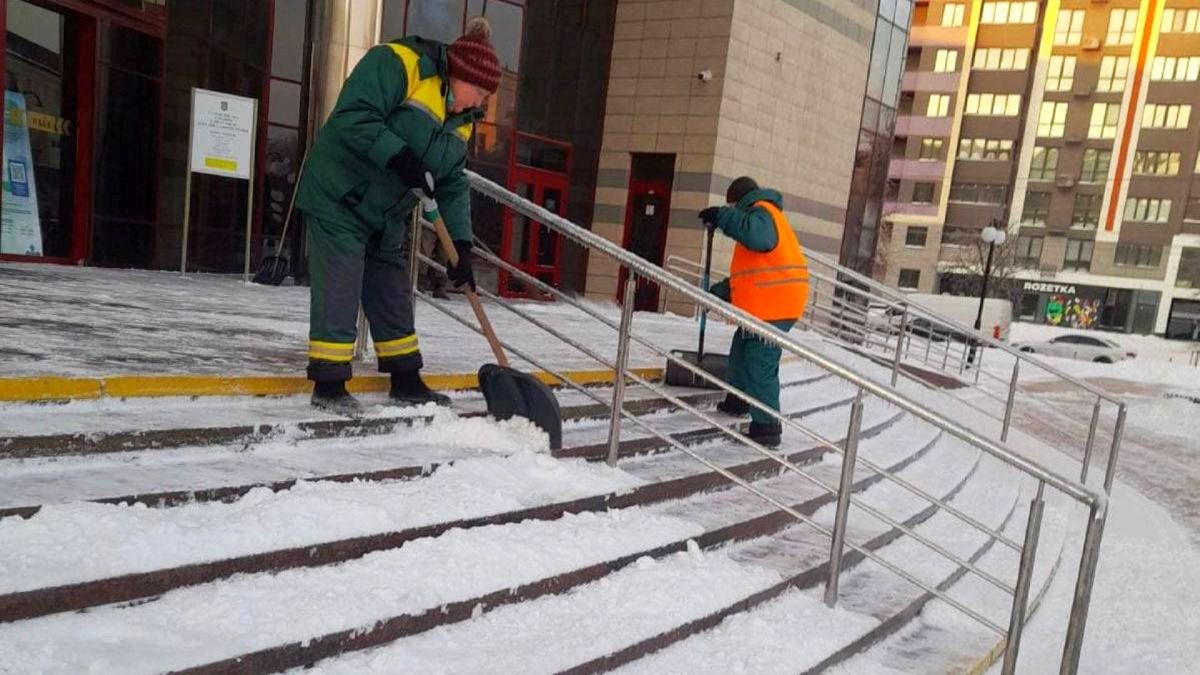 Майже 2000 порушень: у Києві підбили підсумки контролю за прибиранням снігу Двоє комунальників у спецодязі прибирають сніг лопатами на сходах біля громадської будівлі в Києві