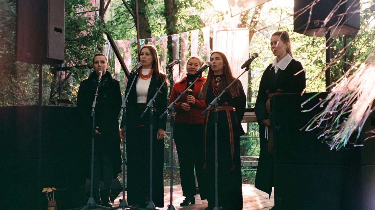 П'ять співачок у темному одязі з намистом і рушниками співають у мікрофони на сцені концерту СМИК.Весна в Києві