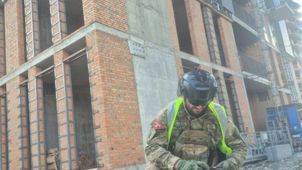 Співробітник НПУ у захисному спорядженні оглядає уламки ворожого безпілотника біля зруйнованої будівлі в Києві після денної атаки дронів 28 квітня 2026 року