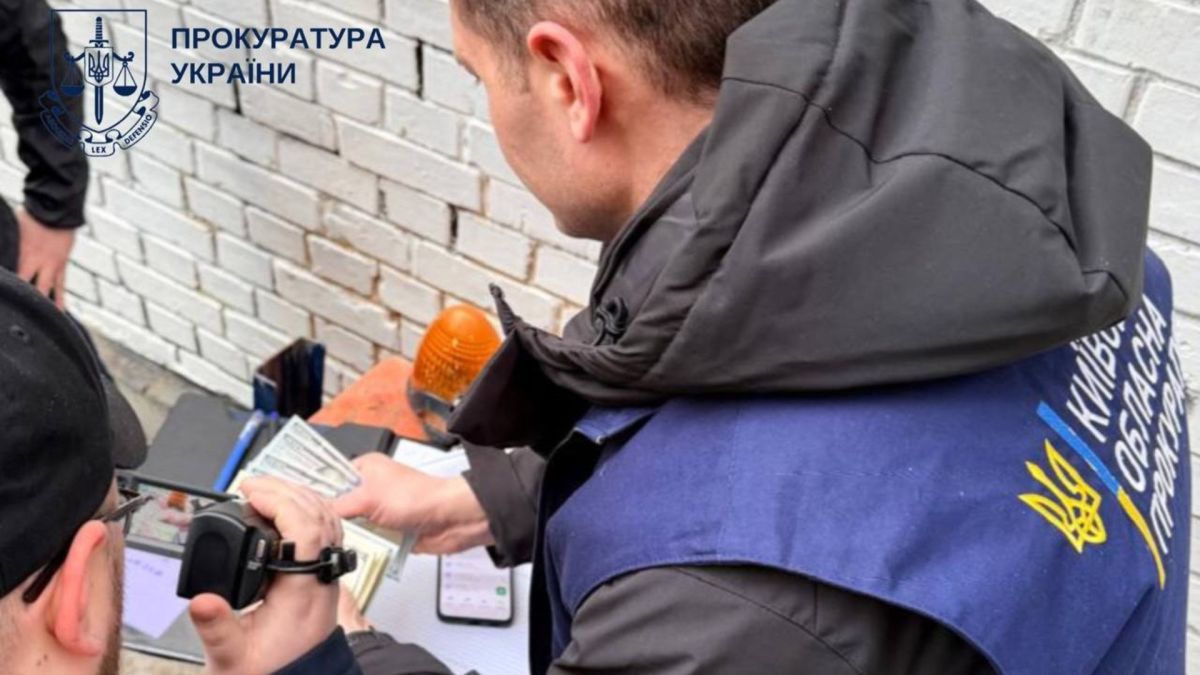 У Києві затримали начальника відділу ДПС за вимагання $500 щомісяця Представник Київської обласної прокуратури у синьому жилеті оглядає вилучені долари США під час затримання начальника відділу ДПС за вимагання хабаря