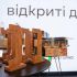 Головні новини Києва | Kyiv.News Дерев’яні статуетки нагороди «Відкриті двері» за безбар’єрні простори на столі на тлі екрана з назвою премії