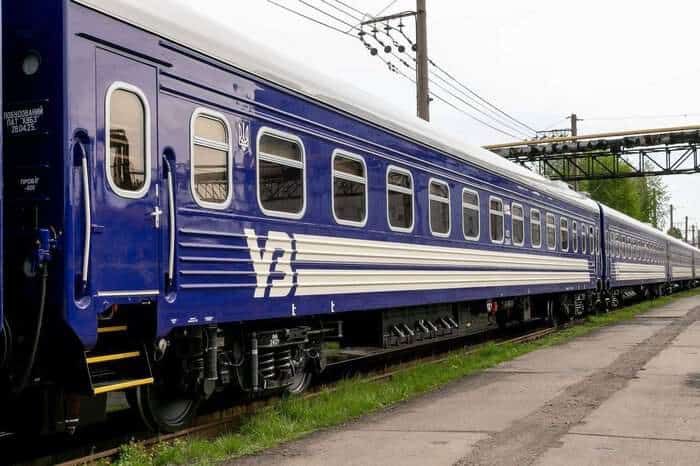 синій пасажирський вагон «Укрзалізниці», що стоїть на залізничній колії
