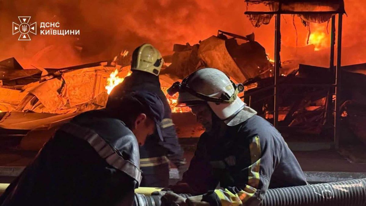На Київщині за ніч загинуло 14 осіб, 27 поранених у трьох районах (оновлено) Двоє рятувальників з'єднують пожежний рукав на тлі масштабної пожежі складських споруд на Київщині
