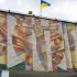Головні новини Києва | Kyiv.News Мозаїчне панно «Мереживо звуків» Василя Хімочки на фасаді ліцею «Престиж» у Боярці: юнак із розкинутими руками серед кольорових променів, над ним прапор України