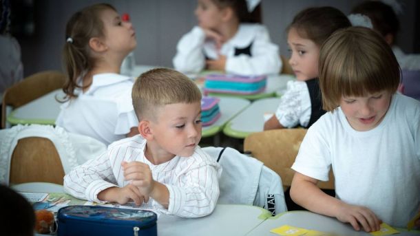 Діти в білих сорочках сидять за партами в класі та займаються творчістю