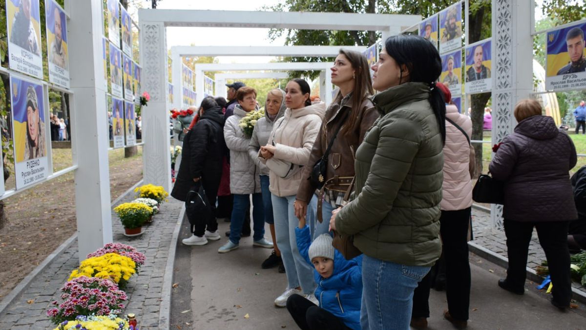 люди стоять на алеї з фотографіями загиблих солдатів ЗСУ, дивляться на фото, осінь