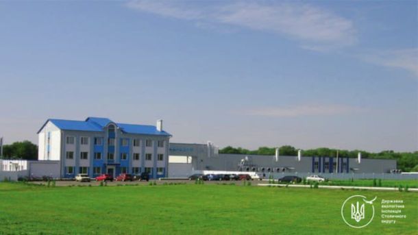 Біло-блакитна адміністративна будівля з синім дахом і виробничий корпус на фоні зеленого поля