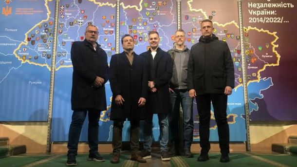 П'ятеро чоловіків стоять на фоні карти України на виставці Національного військово-історичного музею