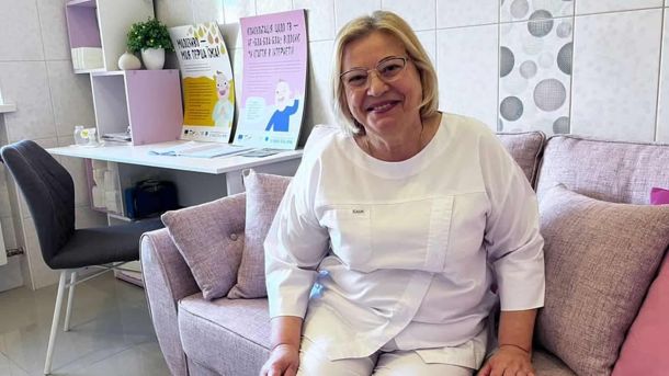 Акушерка у білому медичному халаті сидить на дивані в кабінеті жіночої консультації