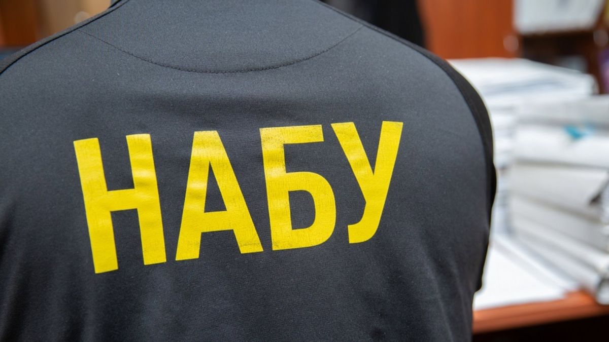 Співробітник НАБУ у темній куртці з жовтим написом НАБУ на спині, на тлі офісного приміщення з документами