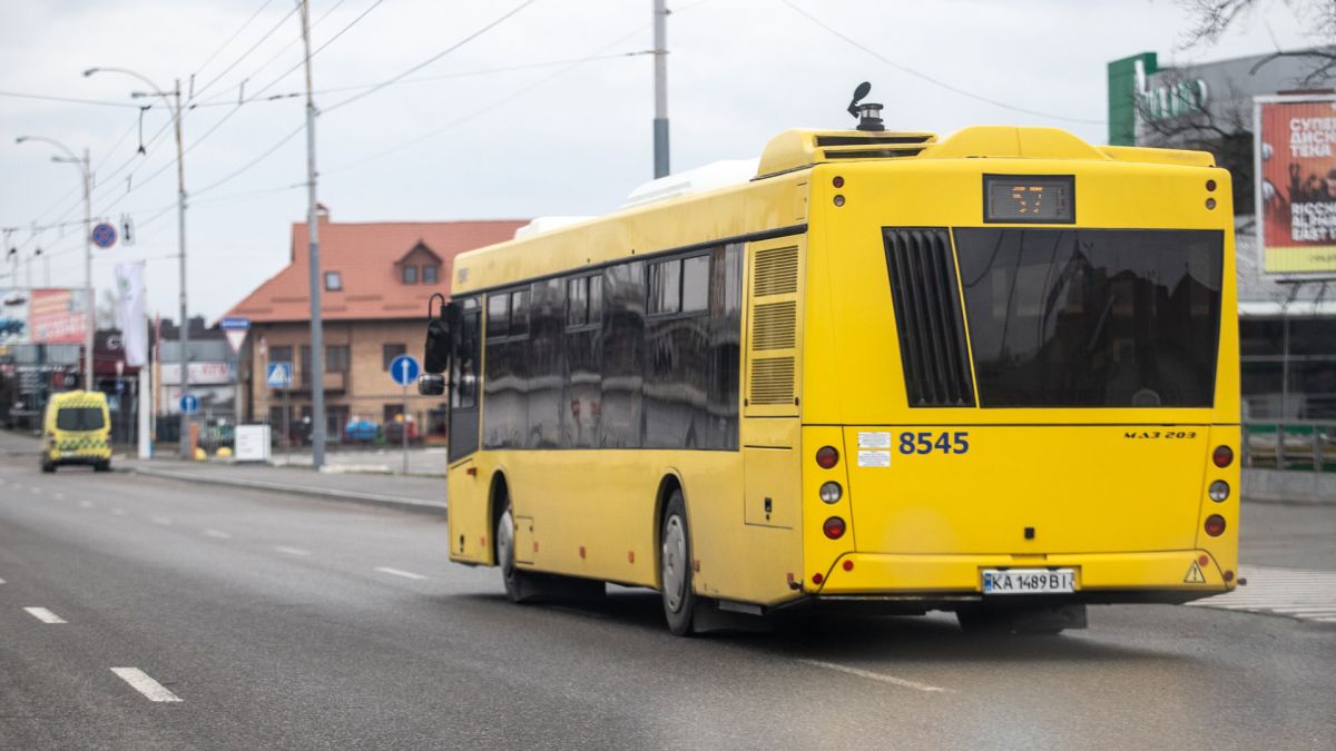 Жовтий міський автобус МАЗ-203 на маршруті в Києві, на задньому плані міська забудова та зупинка громадського транспорту