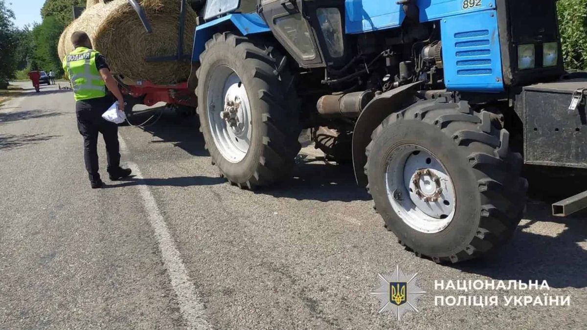 Поліцейський оглядає синій трактор із причепом, завантаженим тюками соломи, на сільській дорозі в Обухівському районі