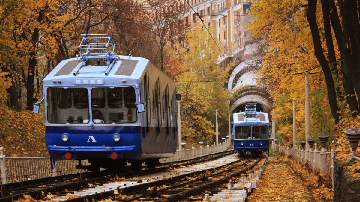 Два синьо-білих вагони київського фунікулера розʼїжджаються на колії серед осіннього листя на Володимирській гірці