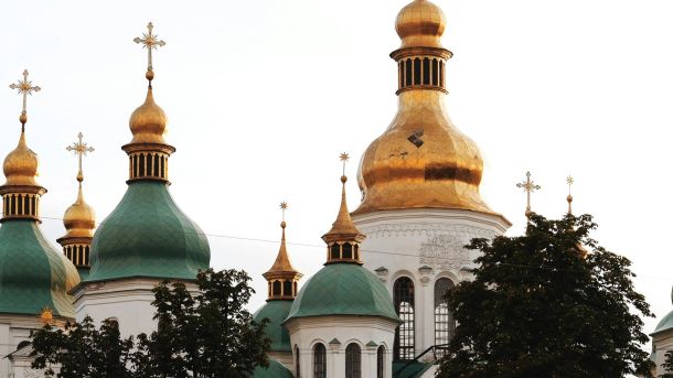 Золоті та зелені куполи з хрестами Софійського собору в Києві на тлі світлого неба