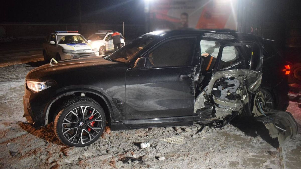 Розбитий чорний BMW X5 M після зіткнення з бетонною опорою на вулиці Івана Виговського в Києві, на задньому плані поліцейський автомобіль