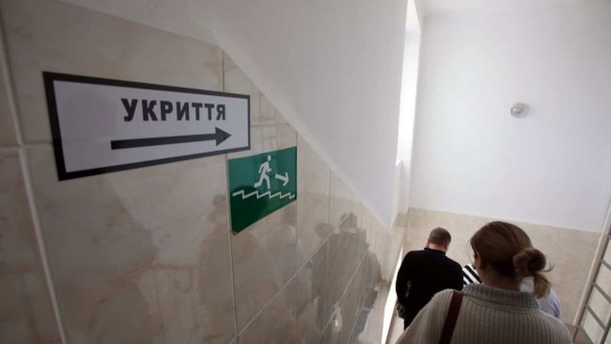 Люди спускаються сходами до укриття повз покажчик з написом «Укриття» під час повітряної тривоги