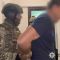 Головні новини Києва | Kyiv.News Спецпризначенець у камуфляжі й шоломі веде затриманого чоловіка з розмитим обличчям у приміщенні