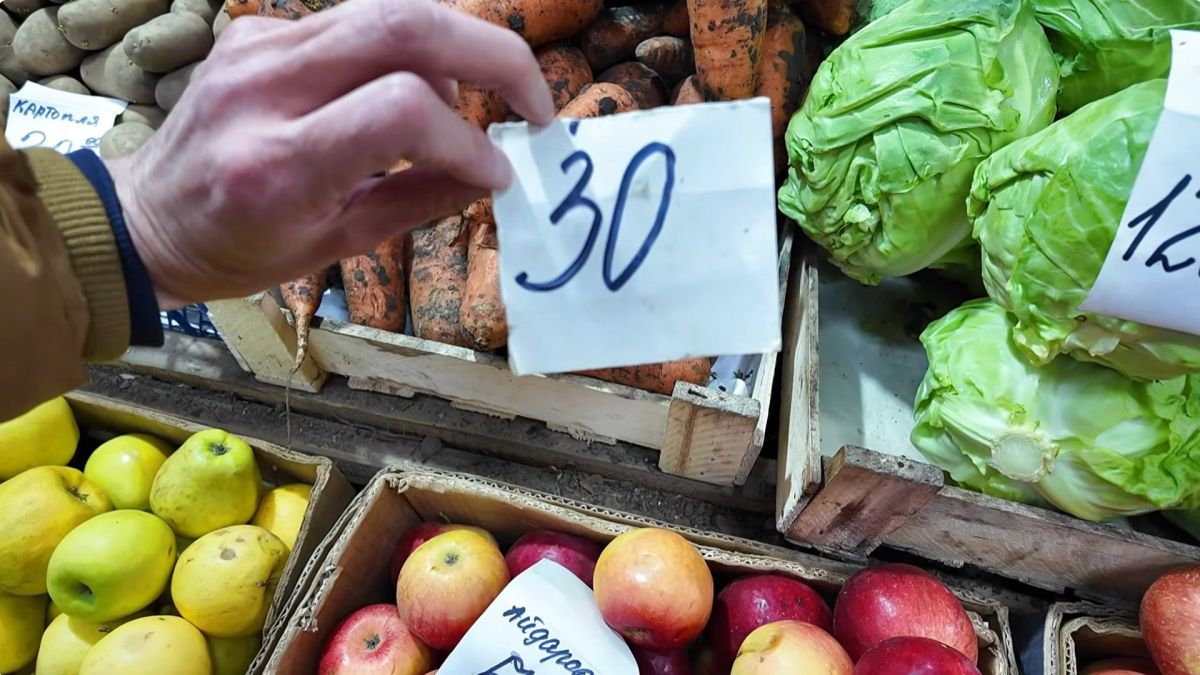 Рука покупця тримає цінник 30 гривень біля моркви та капусти на Лісовському ринку у Києві у квітні 2026 року