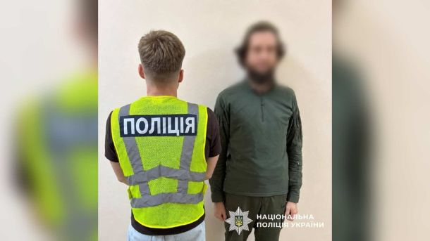Поліцейський у світловідбивному жилеті спиною до камери поруч із чоловіком із розмитим обличчям — підозрюваним у погрозах головному рабину