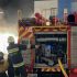 Рятувальники ДСНС розмотують пожежний рукав біля автоцистерни на тлі великого стовпа чорного диму й полум'я над будівлею