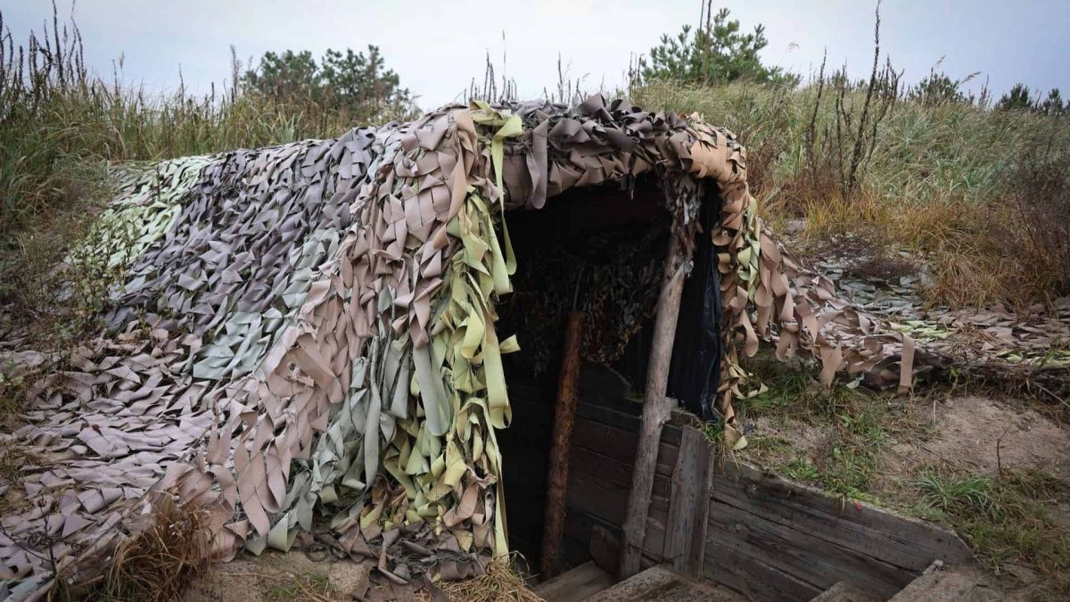 Військовий бункер з камуфляжною сіткою, частково занурений у землю серед трави