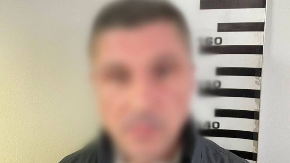 Поліцейське фото затриманого підозрюваного з розмитим обличчям на тлі ростоміра, чоловік у темному одязі