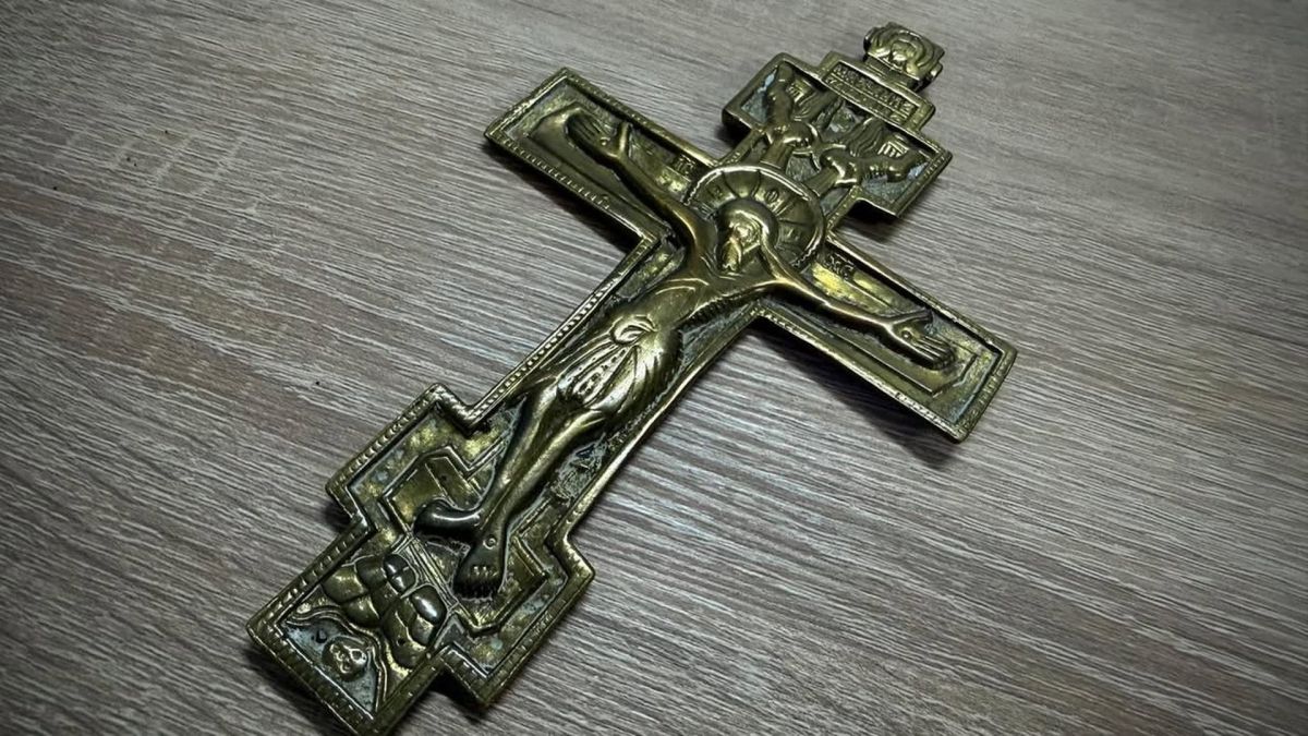 Мідний восьмикінцевий хрест-розп’яття зі старовинним рельєфом на сірій дерев’яній поверхні — один із предметів, вилучених Київською митницею
