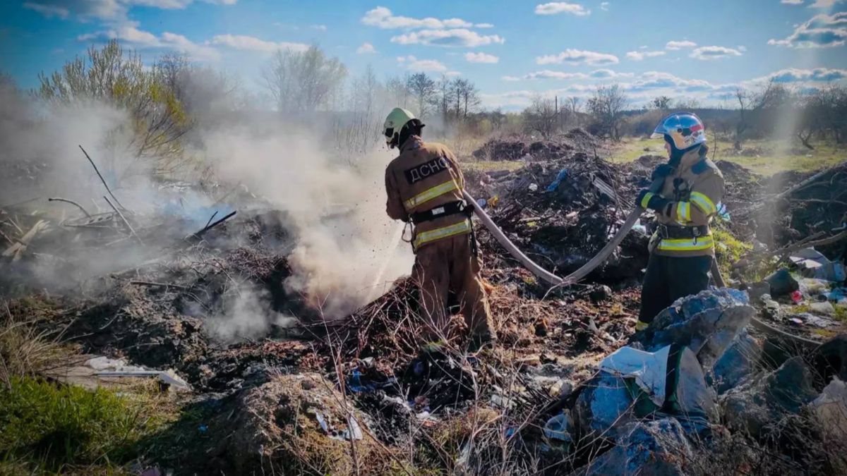Двоє рятувальників ДСНС у спорядженні гасять пожежу сухої рослинності та сміття на відкритій території Бучанського району