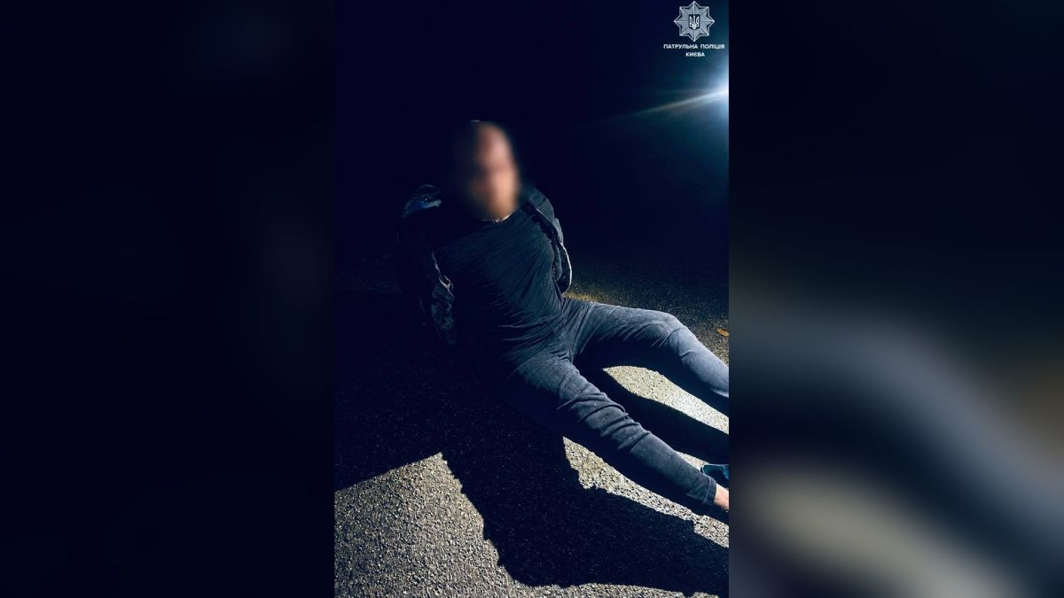 Затриманий патрульними чоловік із розмитим обличчям сидить на нічному асфальті в Києві