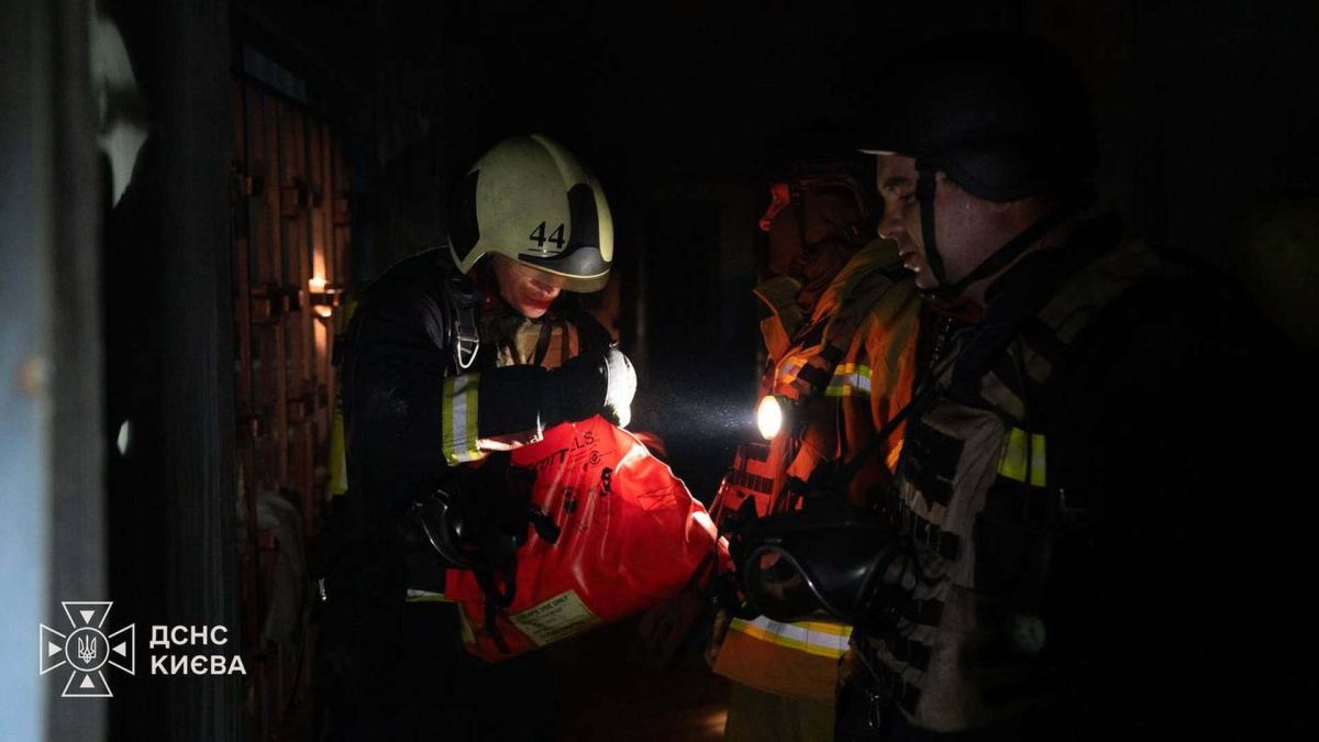 Двоє рятувальників ДСНС у захисному спорядженні з помаранчевою рятувальною сумкою в темному задимленому приміщенні під час гасіння пожежі