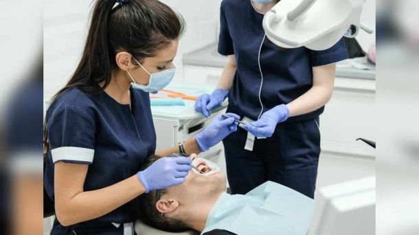 Стоматологиня з асистенткою лікують пацієнта у стоматологічному кабінеті — ілюстрація до переліку безоплатних стоматологічних закладів Києва