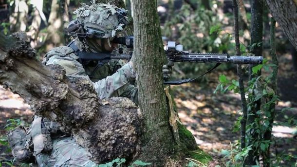Військовий сидить в лісосмузі з гвинтівкою і прицілюється