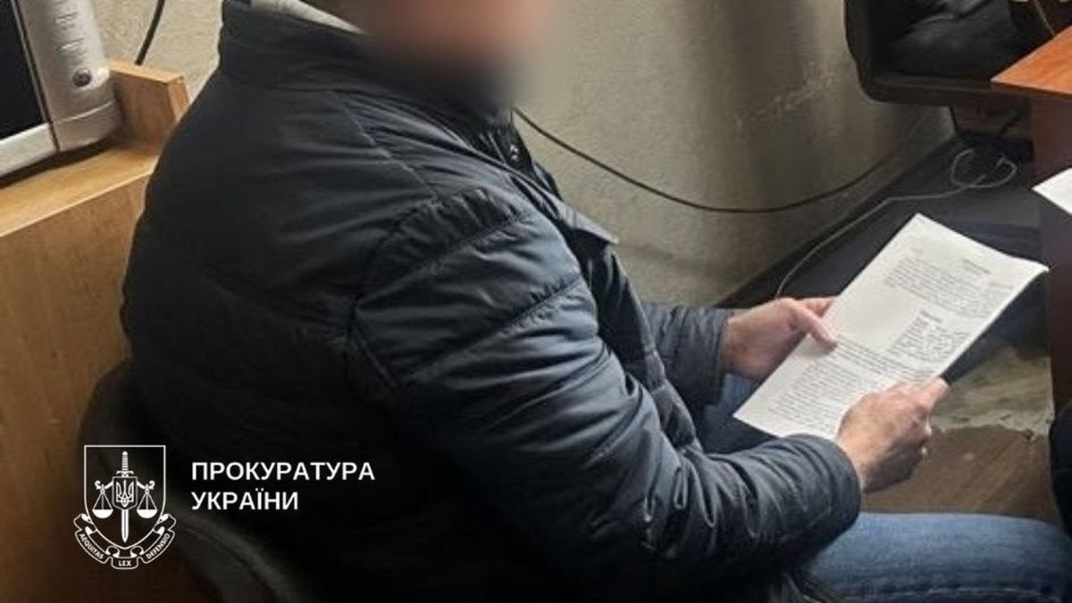 Чоловік в чорній куртці сидить на стільці і тримає папери