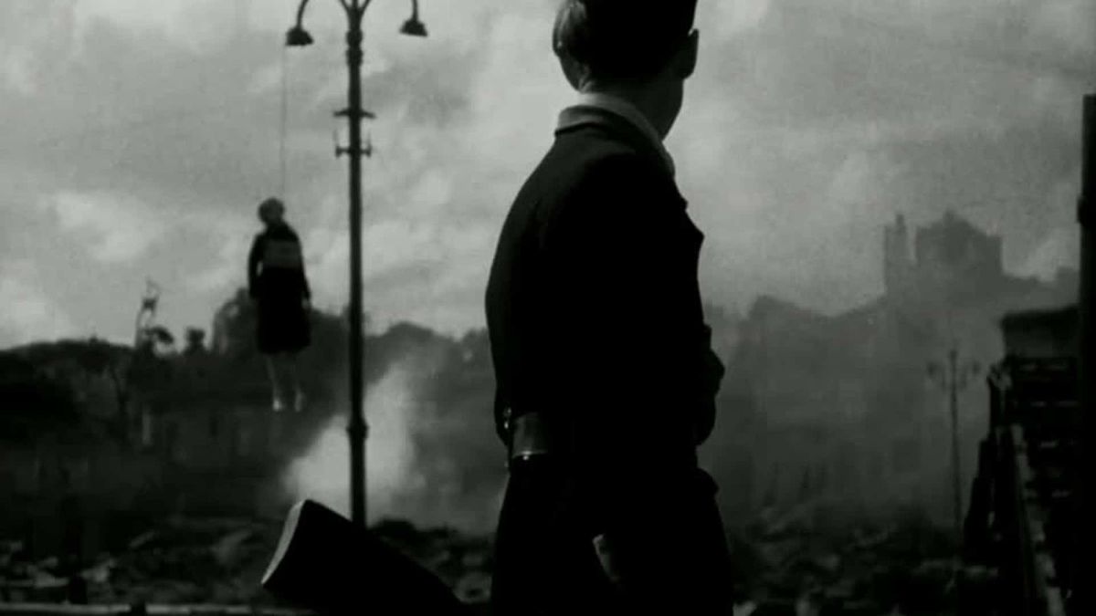 Чорно-білий кадр із фільму «Нескорені» (1944): силует солдата з рушницею на тлі зруйнованого міста і диму, чоловік у формі стоїть спиною до глядача