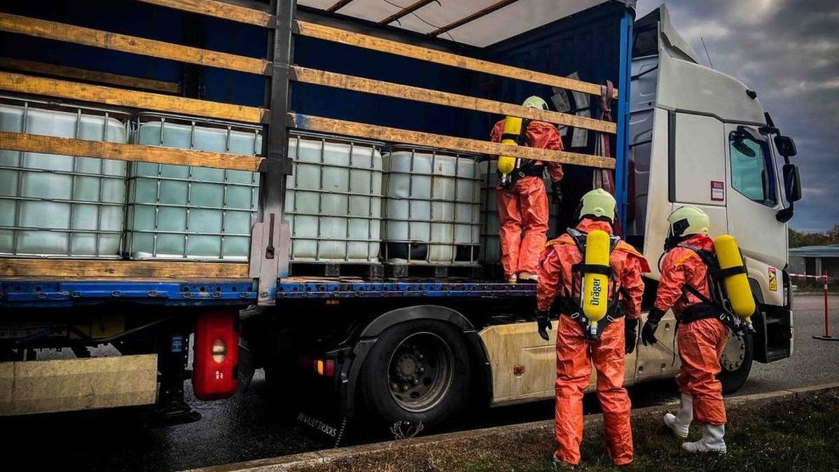 Троє людей у захисних костюмах оглядають вантажівку з великими пластиковими ємностями