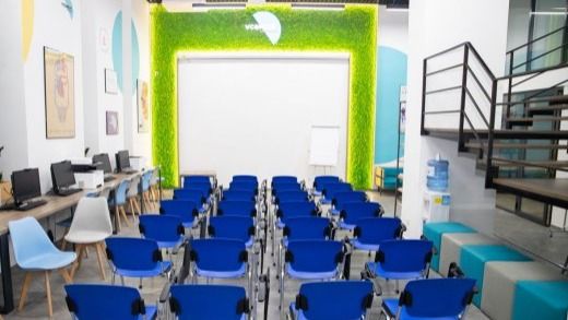 Сучасна лекційна зала з рядами синіх стільців, розташованих перед великою білою стіною-екраном, обрамленою зеленою декоративною панеллю