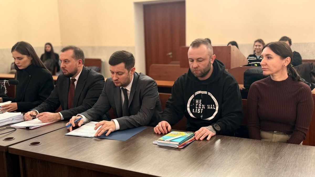 Учасники судового засідання у справі Olympic Village сидять за столом у залі Києво-Святошинського районного суду, прокурори переглядають документи