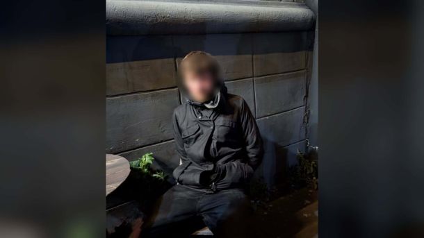 Чоловік у темній куртці з розмитим обличчям сидить біля стіни після затримання за підозрою в розбої в кав’ярні в Києві