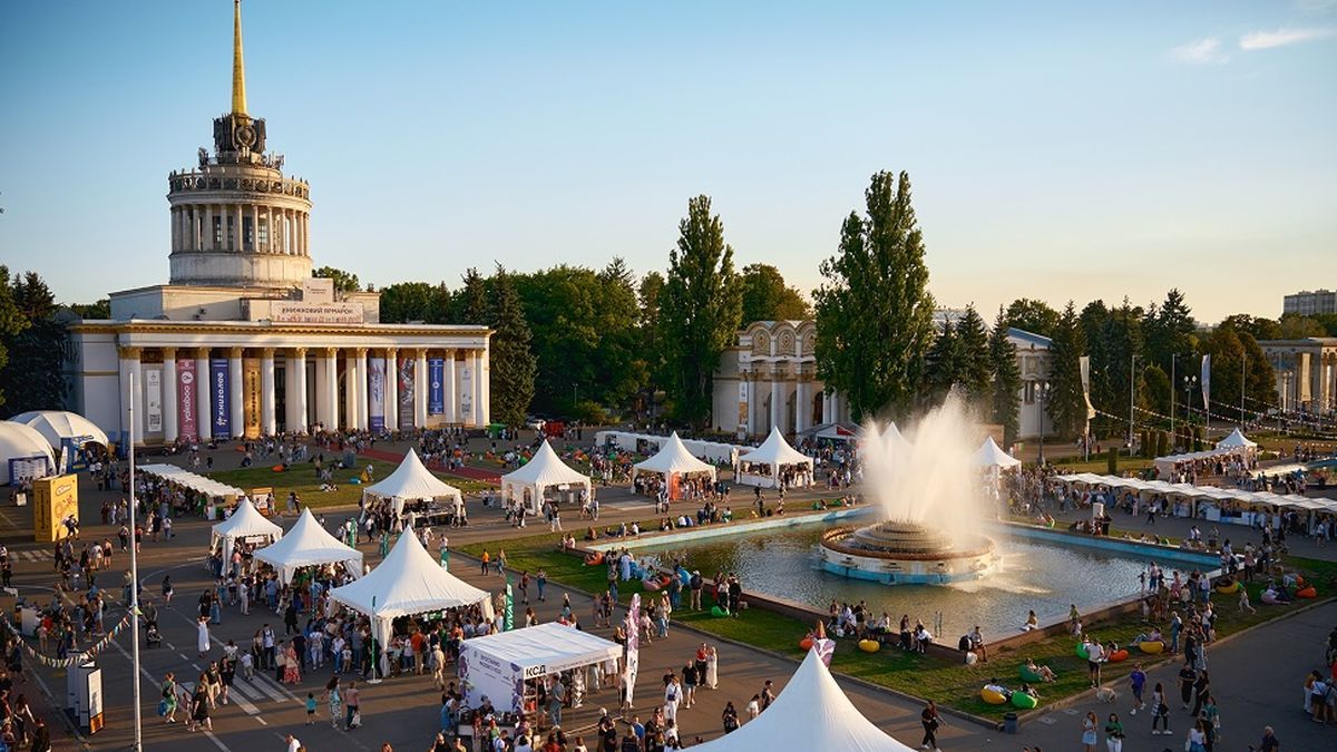 Виставковий центр у Києві з колонами та шпилем, перед ним площа з великим фонтаном і білими шатрами
